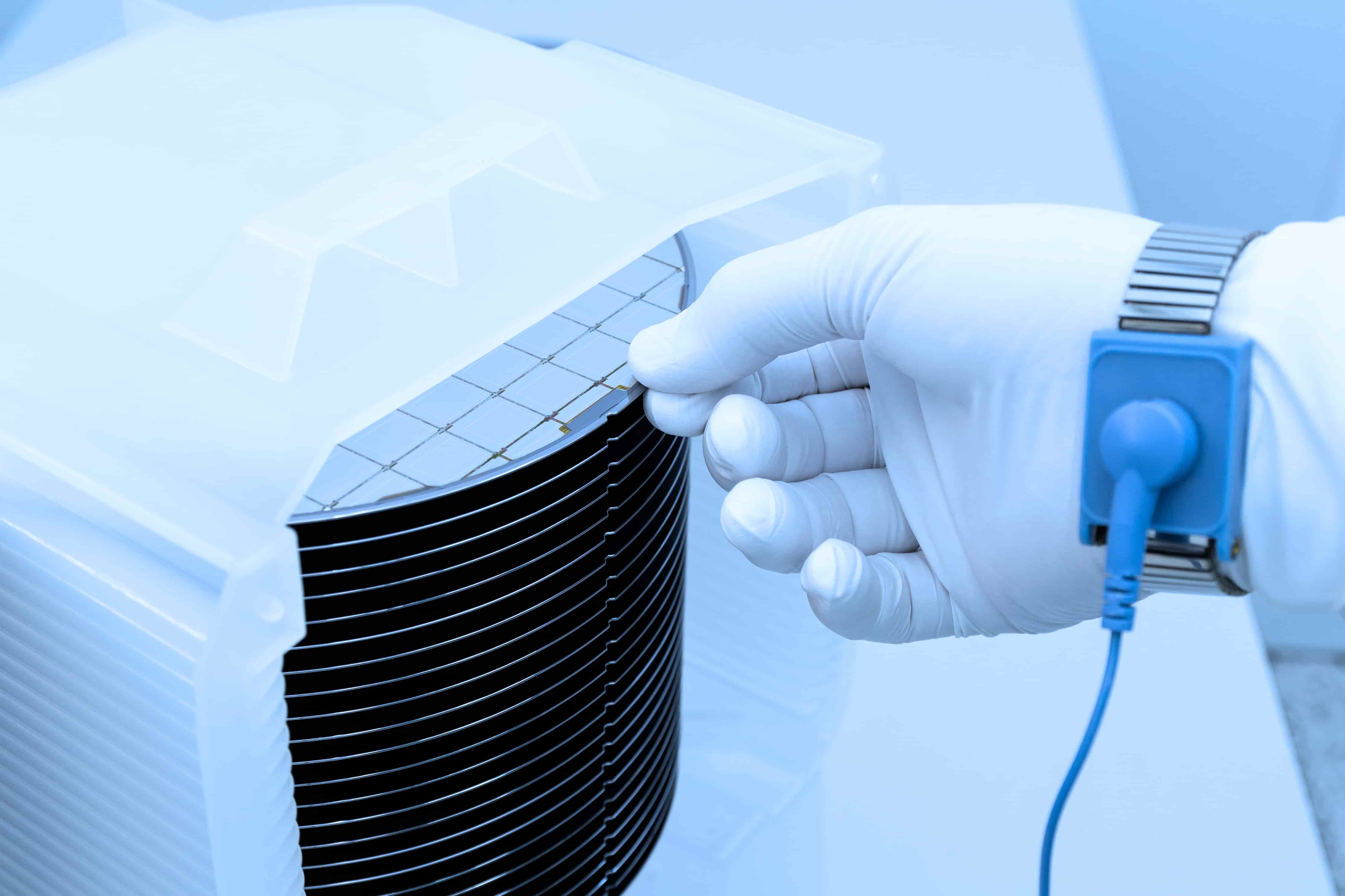 Hand mit weißen Nylon-Handschuhen entnimmt vorsichtig einen Siliziumwafer aus einer Reinraum-Aufbewahrung