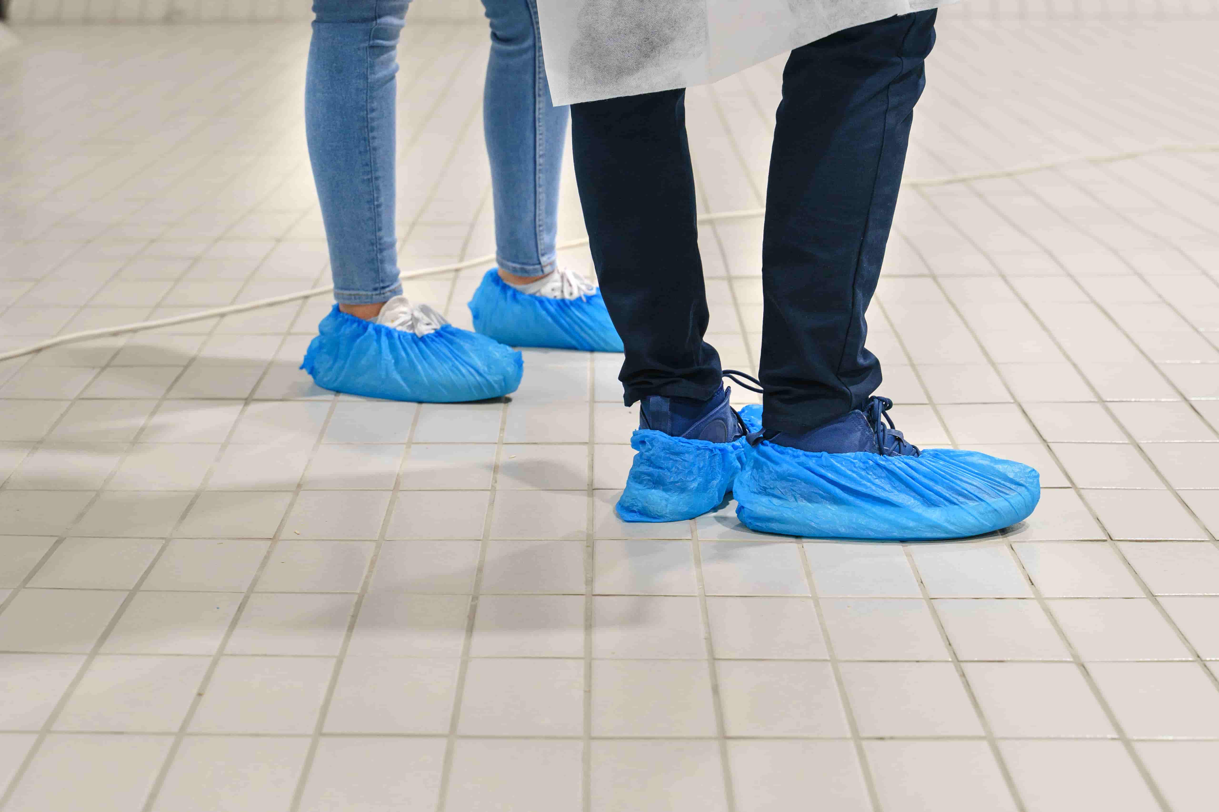 Personen tragen blaue Überziehschuhe als Hygieneschutz in Innenräumen